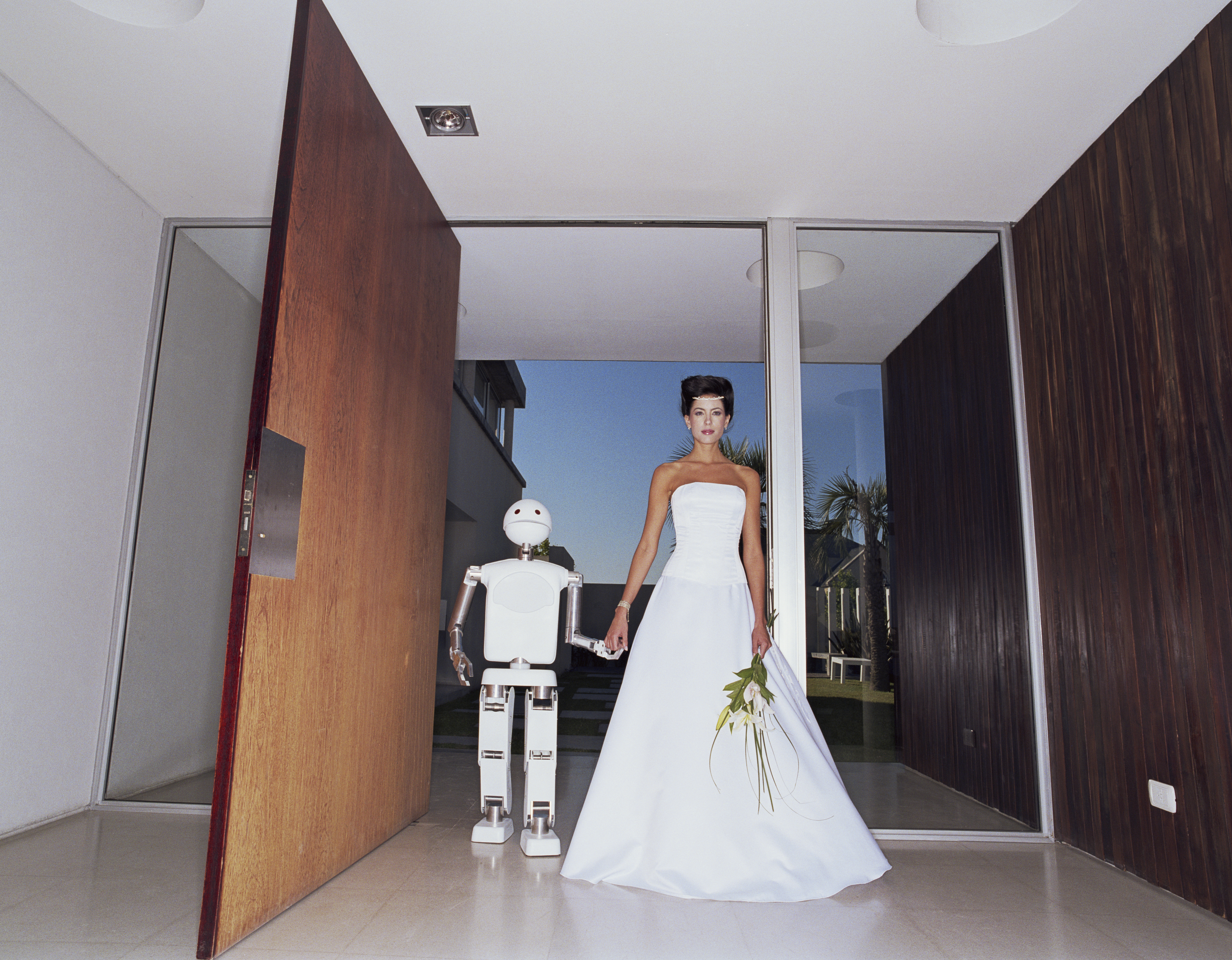 Bride and robot holding hands in entryway of house, portrait